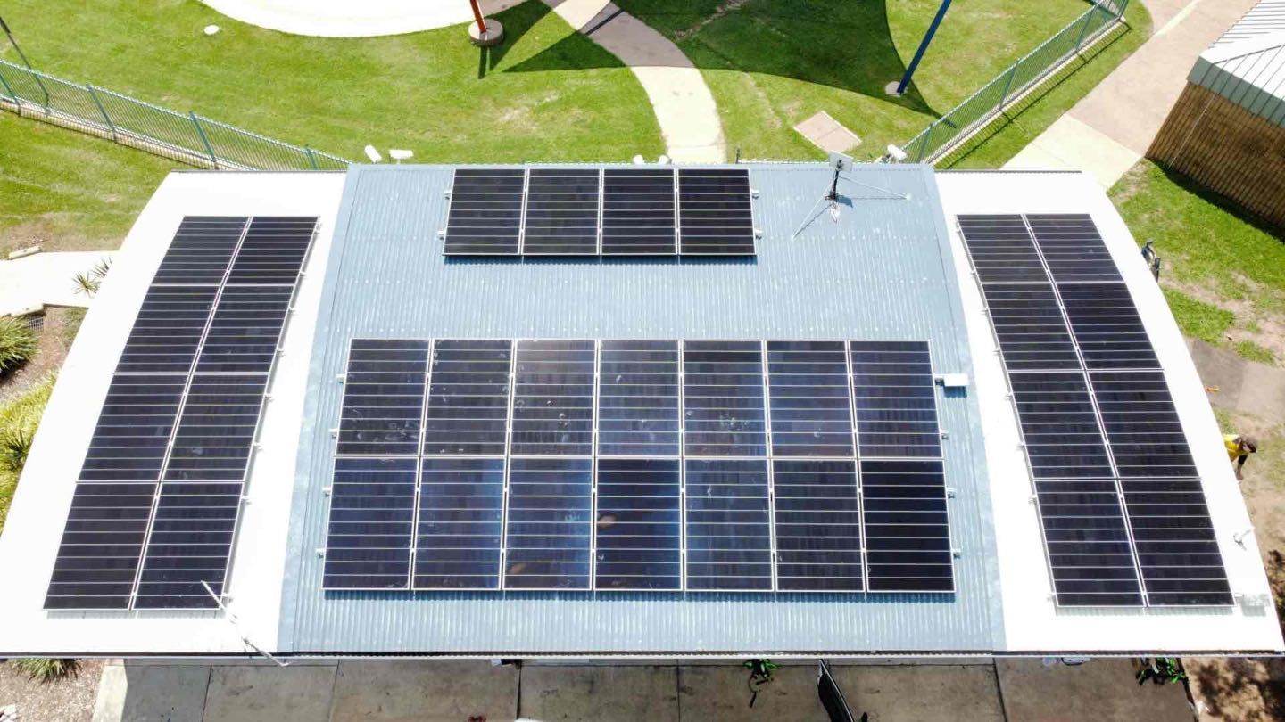 Rooftop with multiple solar panels on a white roof, viewed from above.