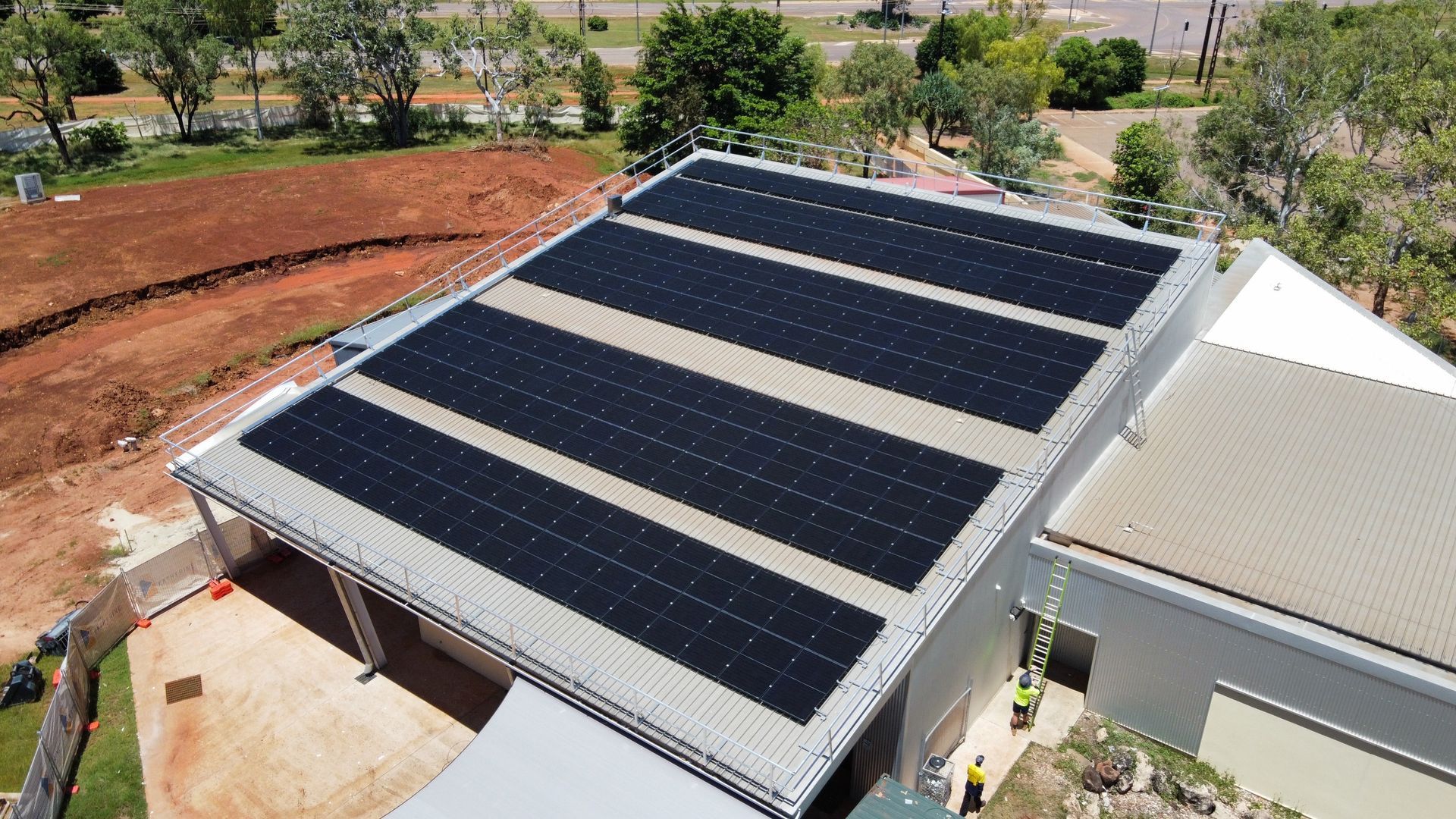Aerial view of a house roof with large black solar panels in a sunny outdoor setting