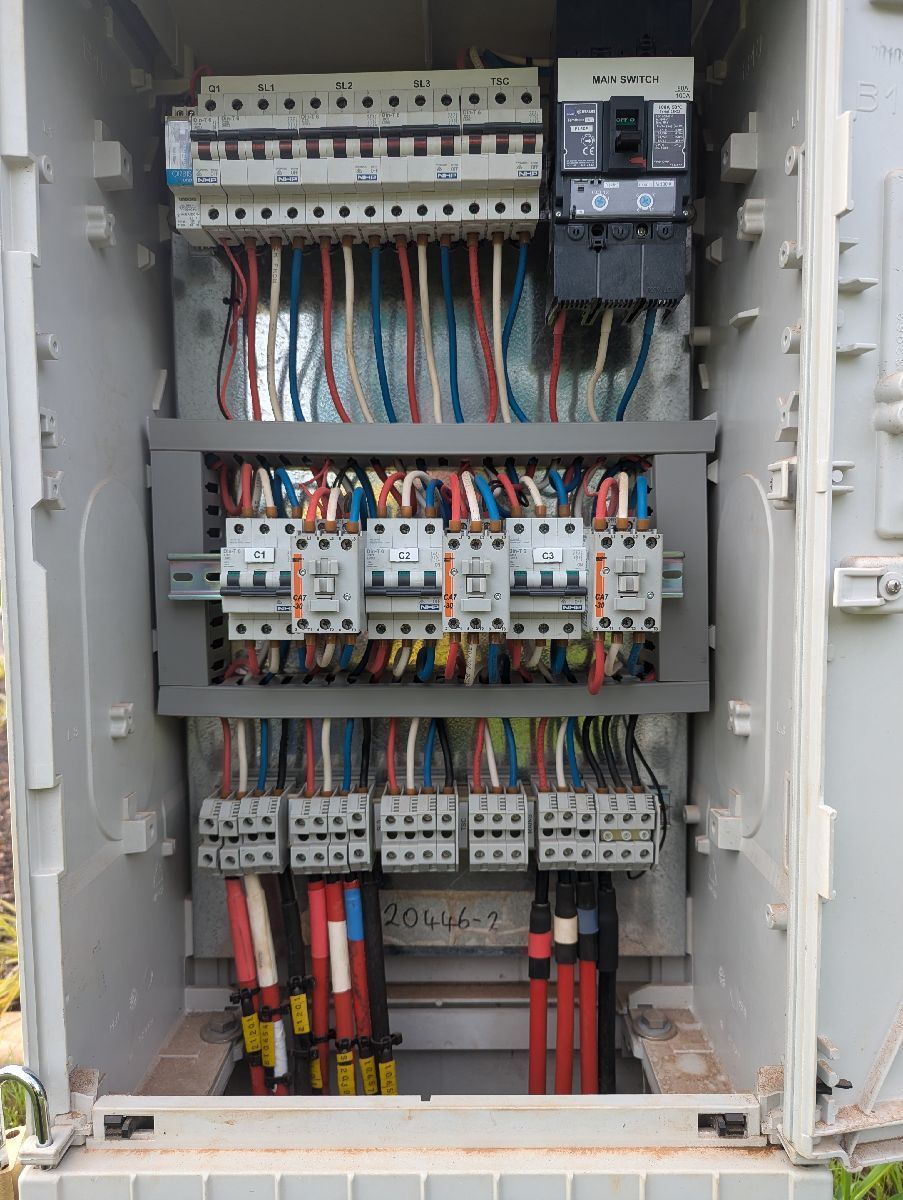 Open electrical control panel with rows of circuit breakers, relays, and colored wiring.