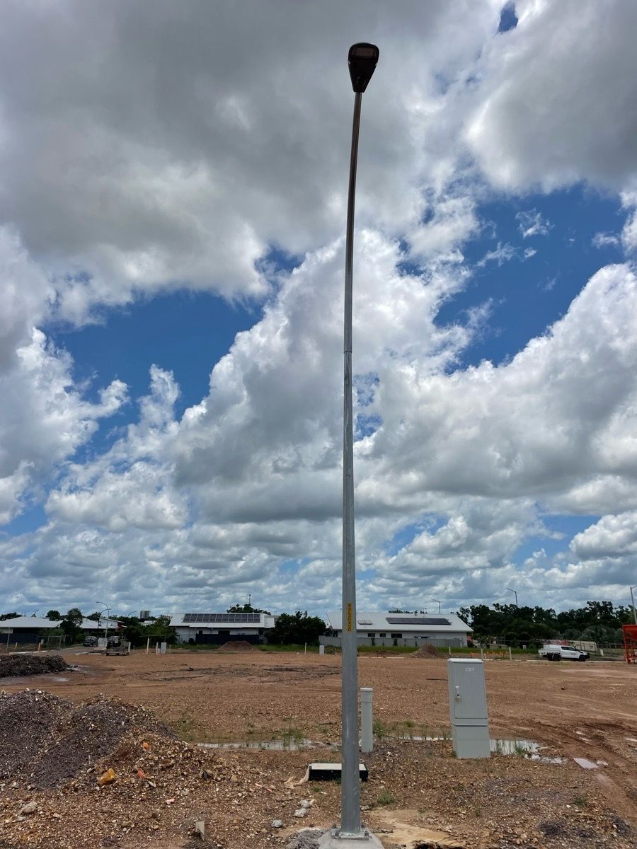 Tall streetlight on a dirt lot under a cloudy sky, with small utility boxes nearby.