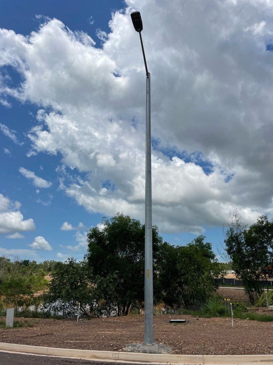 Tall streetlight pole against a cloudy blue sky in a landscaped area