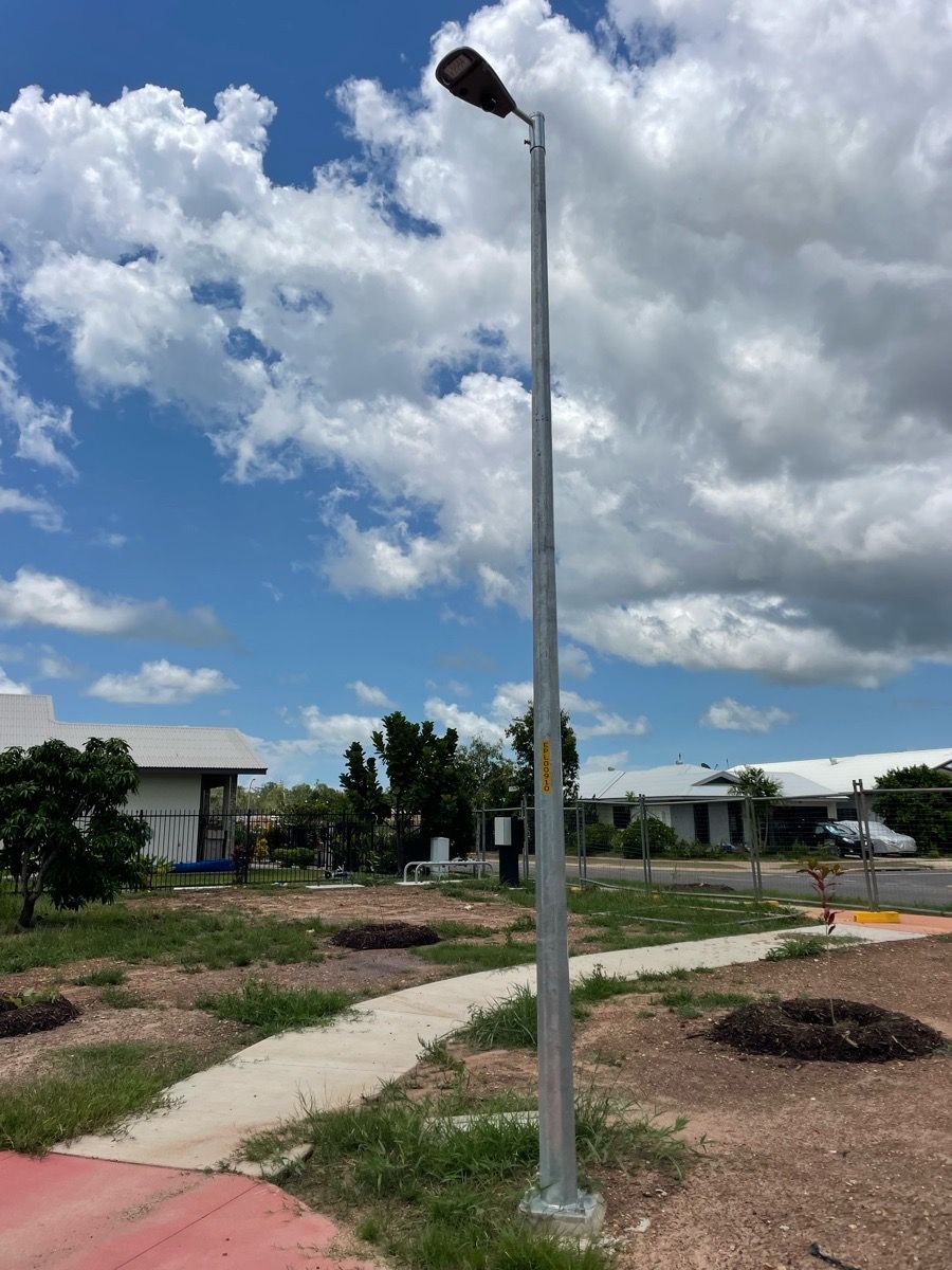 Tall streetlight on a paved path in a vacant outdoor area under a cloudy blue sky.