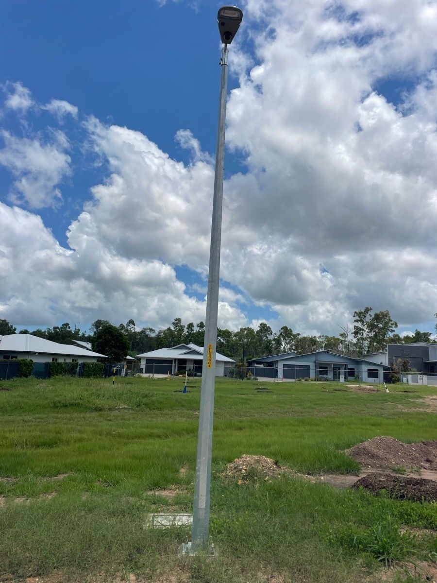 Tall streetlight in a grassy field with houses under a partly cloudy sky