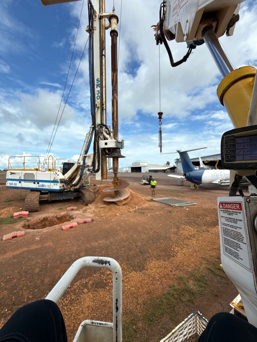 Construction crane beside large airplane on a muddy airport worksite, with a worker in safety gear nearby