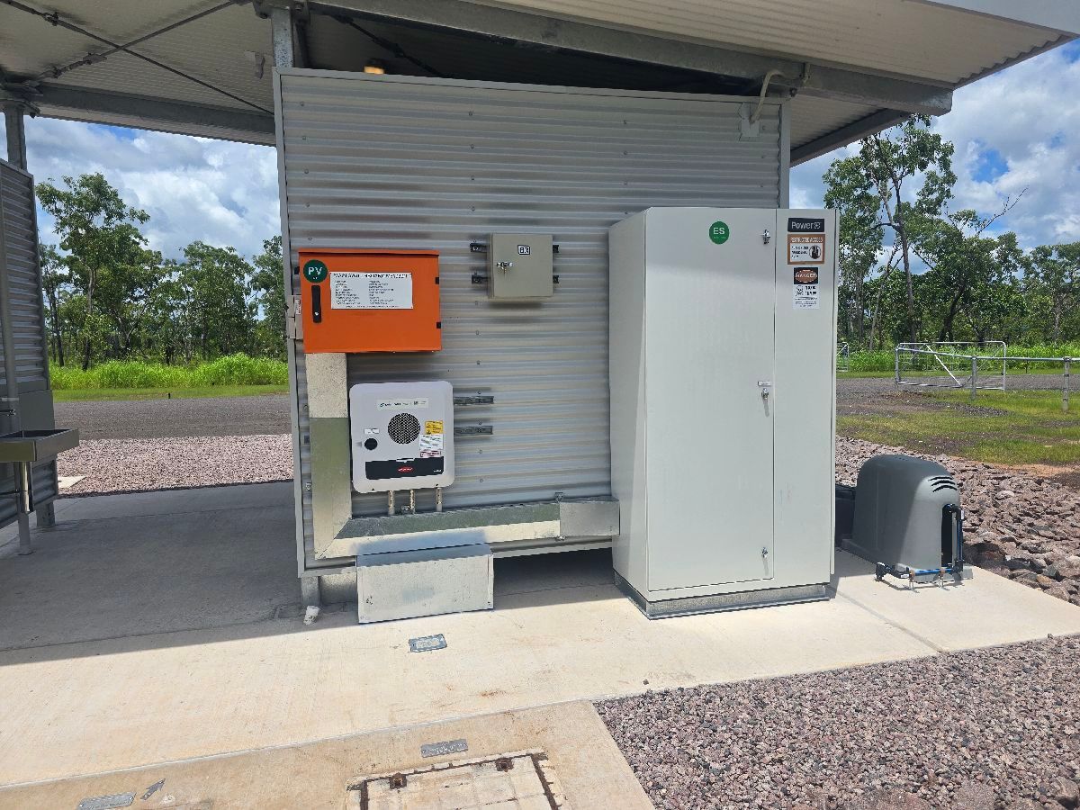 Outdoor utility station with an orange control box, white cabinet, and meter under a metal shelter.