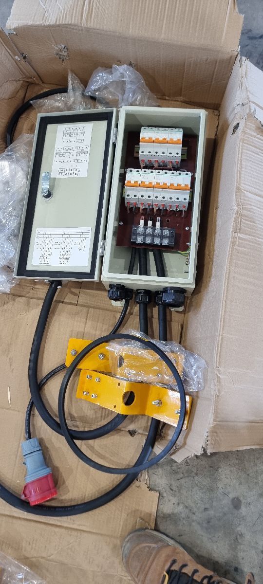 Open electrical control box with wires, breakers, and a yellow cable reel in a cardboard box
