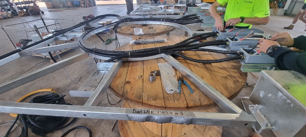 Workers inspect a large circular metal assembly with hoses in a workshop, surrounded by tools and equipment.