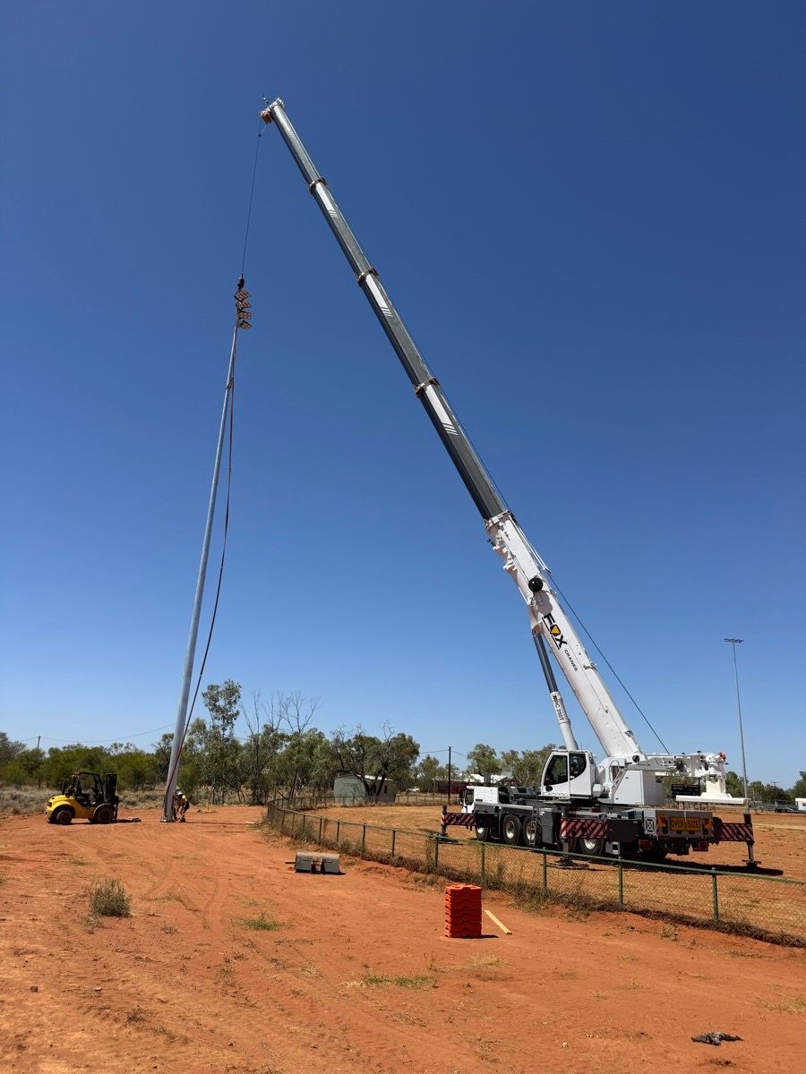 Crane truck lifting a long cable or pole in a dry, open field under a blue sky
