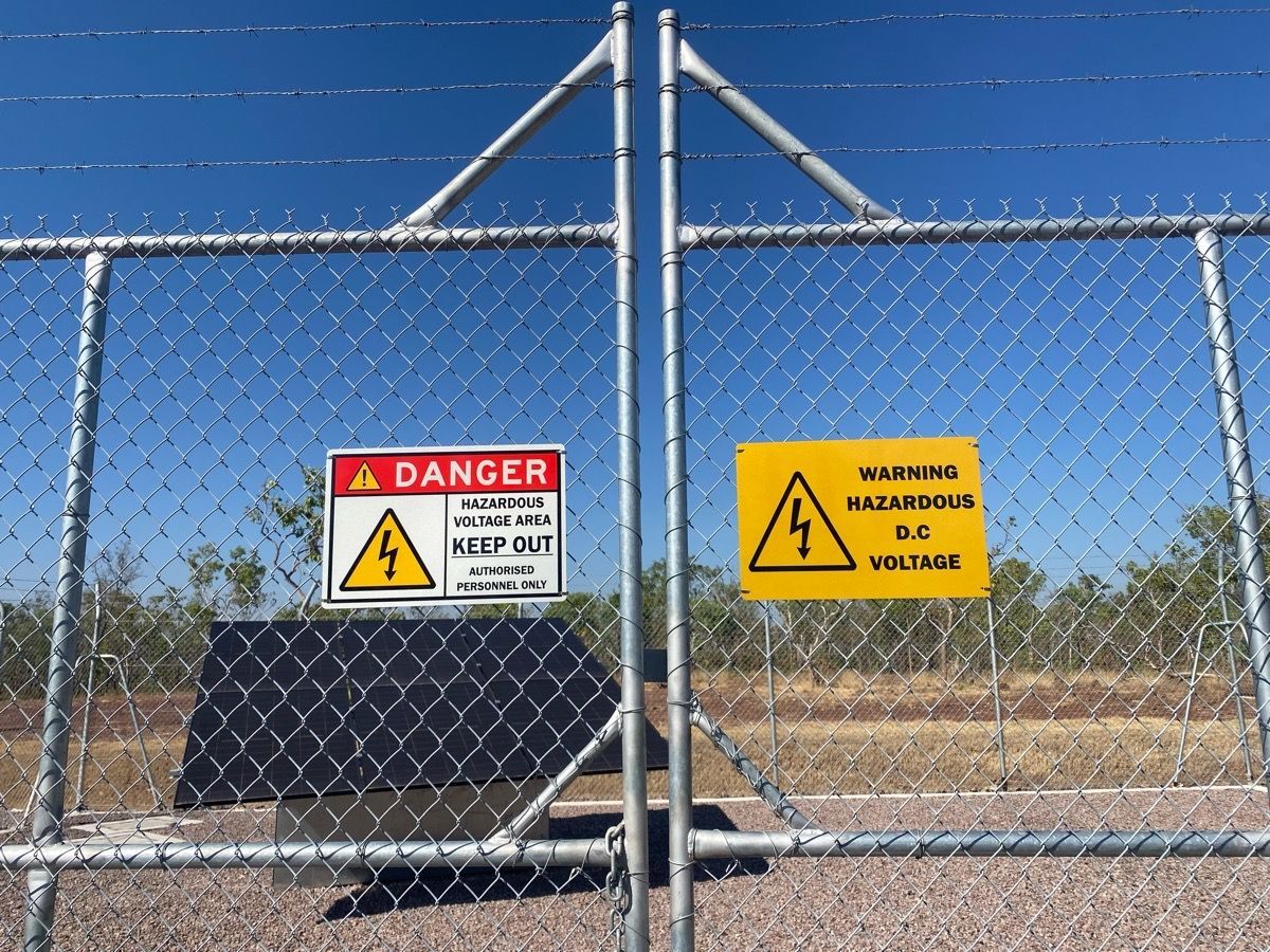 Chain-link fence with red and yellow danger signs at a secured entrance under a blue sky