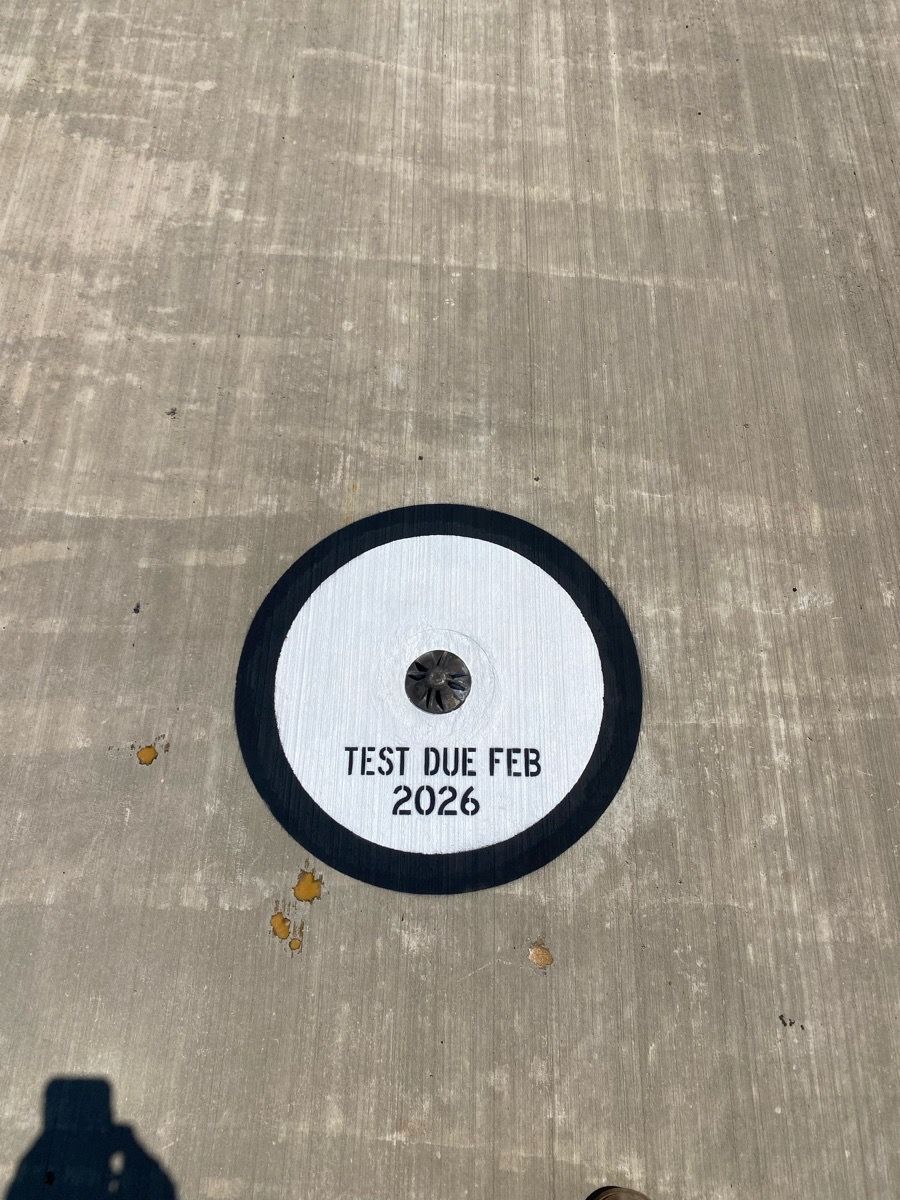 White circular marker on concrete, labeled “TEST DIE FEB 2026” with a black rim and center hole.