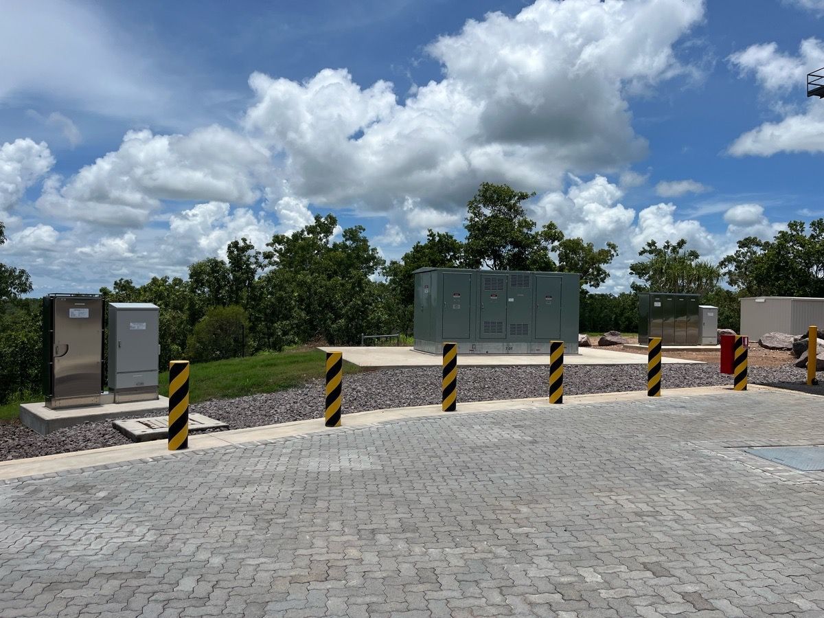 Parking area with striped barriers, utility boxes, and a cloudy sky over green trees