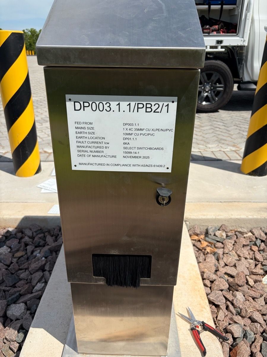 Stainless steel utility box with label and black vent, beside striped pole and gravel walkway outdoors