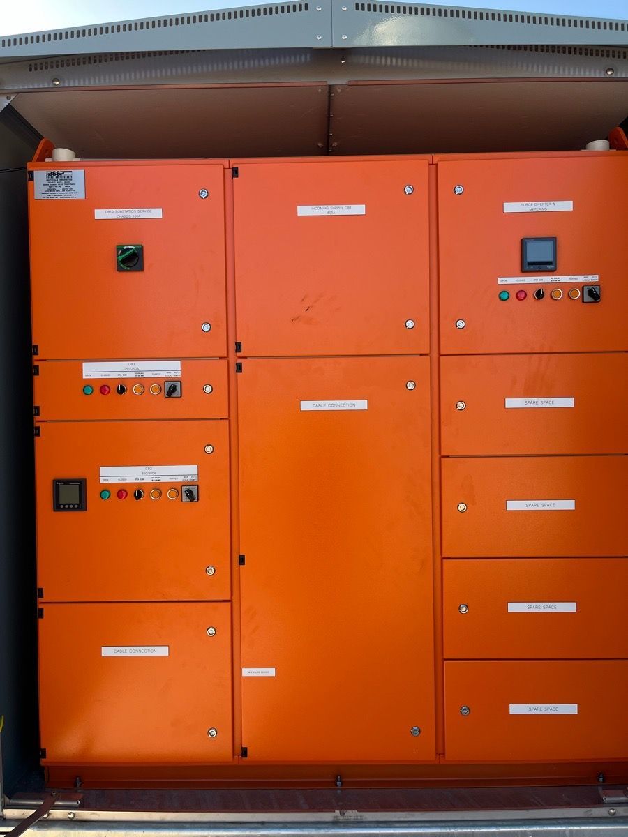 Orange industrial control cabinet with multiple doors, displays, and buttons under a metal canopy