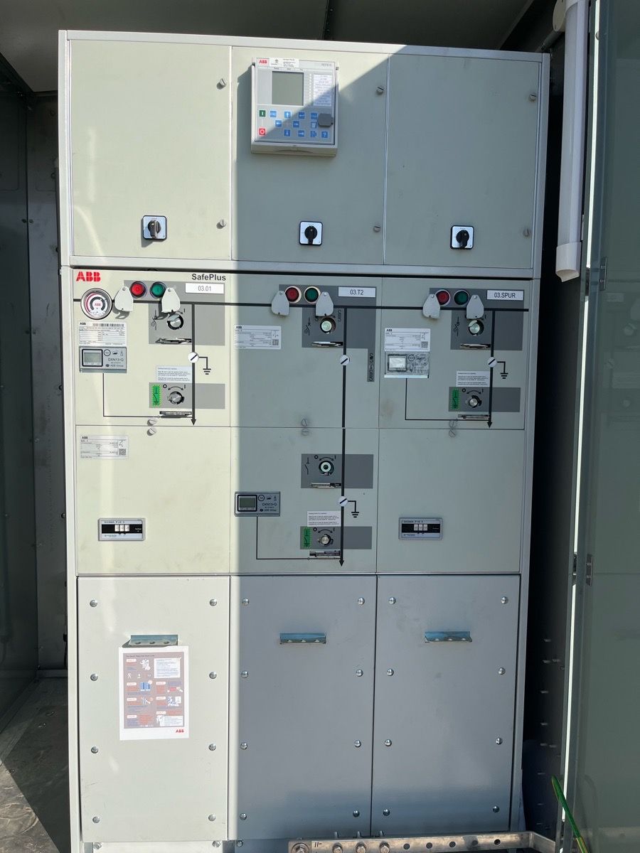 Large gray electrical switchgear cabinet with warning labels and control panels indoors