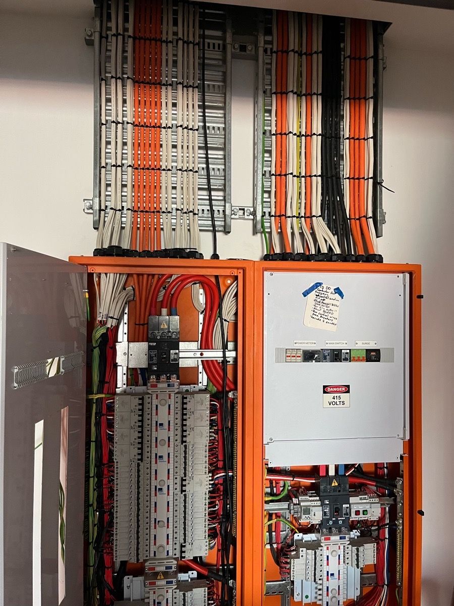 Open electrical control panels with orange frames and rows of wires in a utility room.