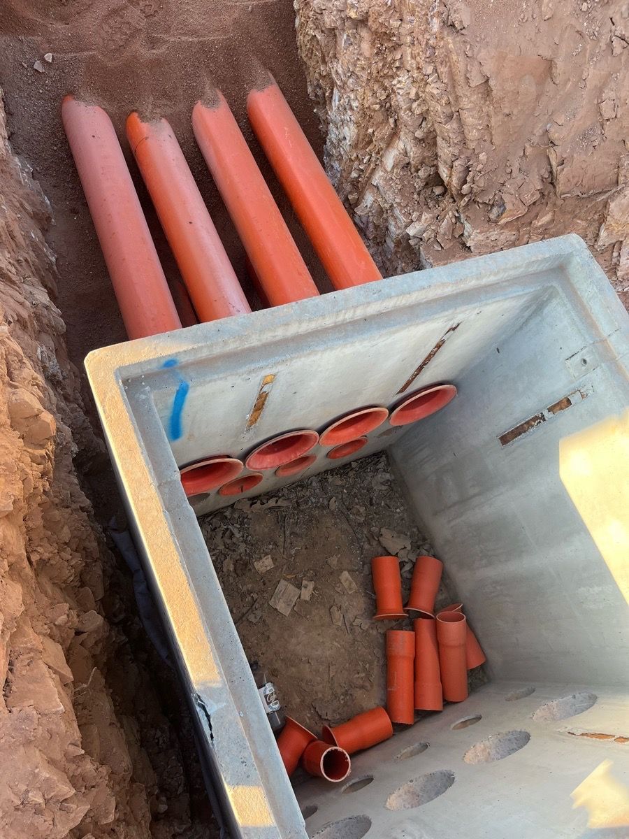 Open concrete utility pit with orange drainage pipes and fittings installed in a trench
