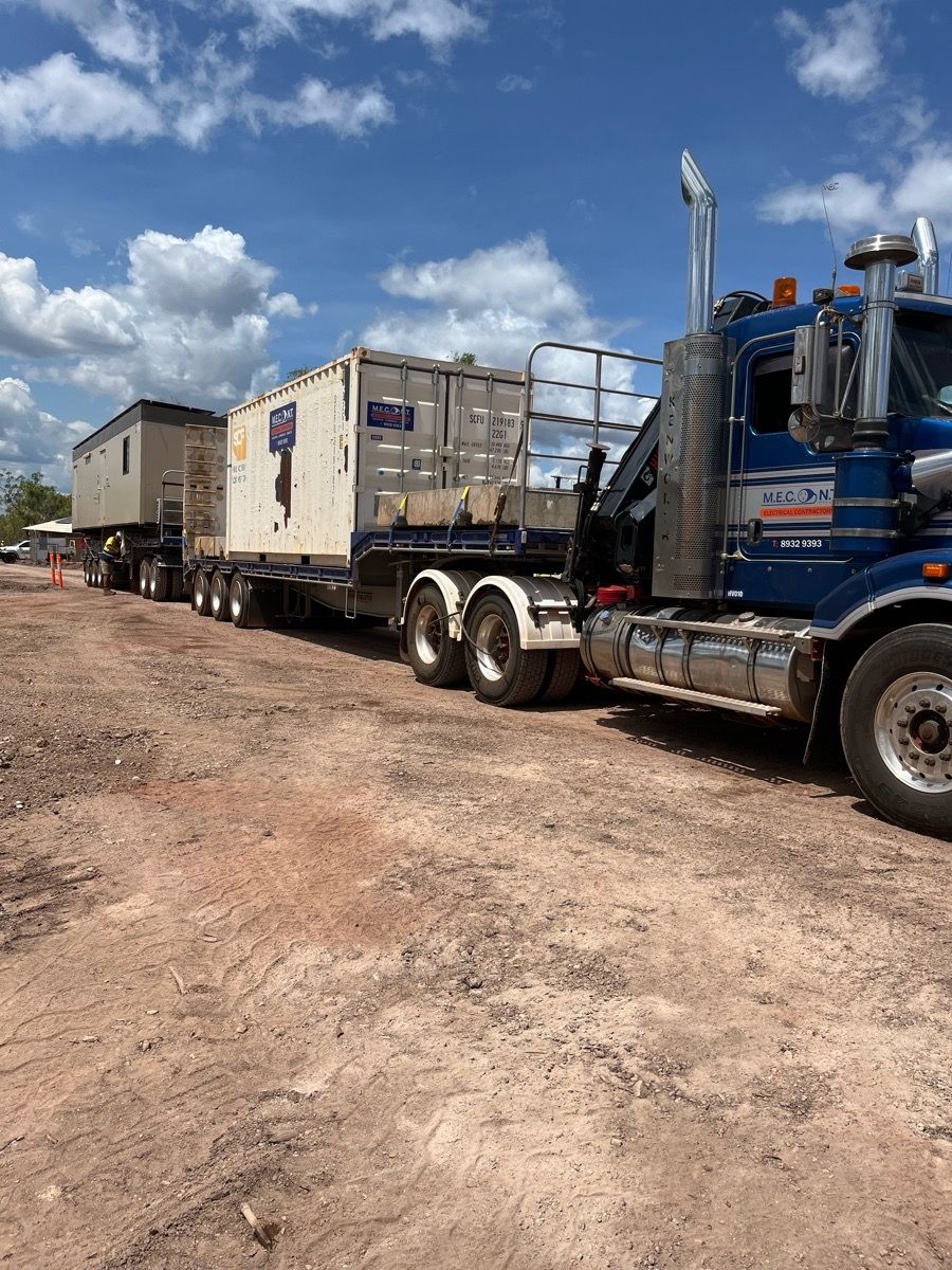 Blue semi truck towing white cargo trailers on a dirt road under a cloudy sky