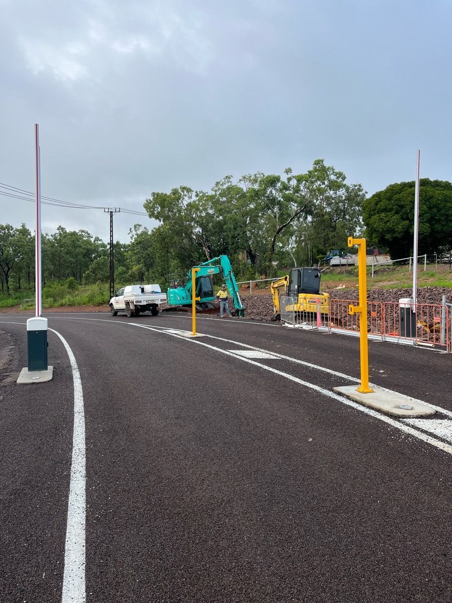 New paved road curves past construction equipment and traffic posts under an overcast sky