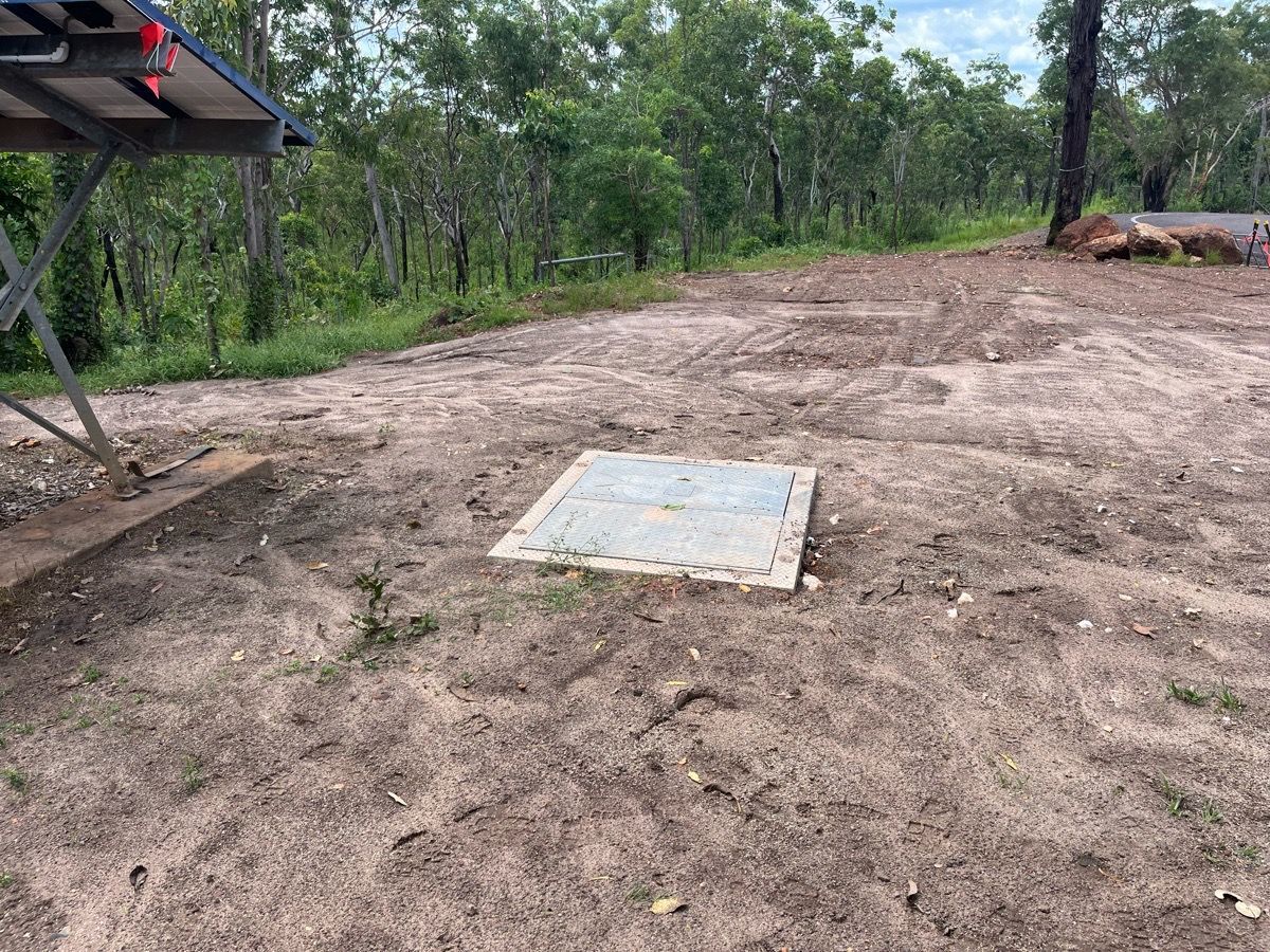 Dirt clearing with a concrete utility cover, surrounded by trees and sparse vegetation