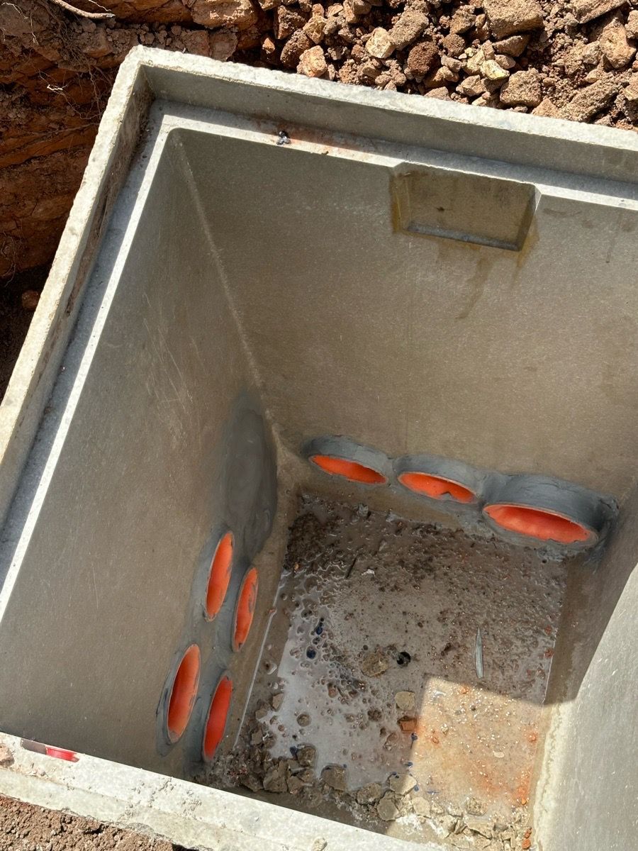 Open concrete utility box with orange cable conduits in a dirt excavation.