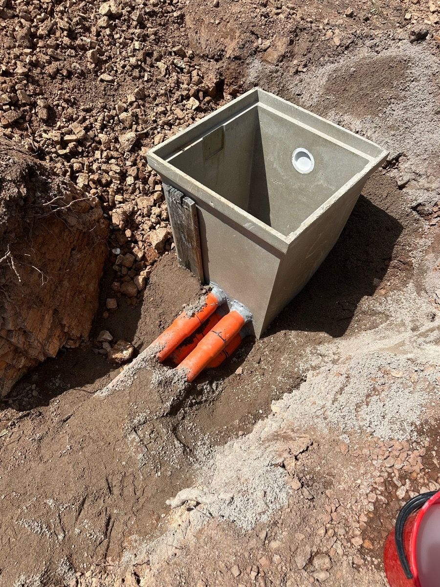 Concrete utility box installed in a dirt trench with orange conduit pipes exposed nearby