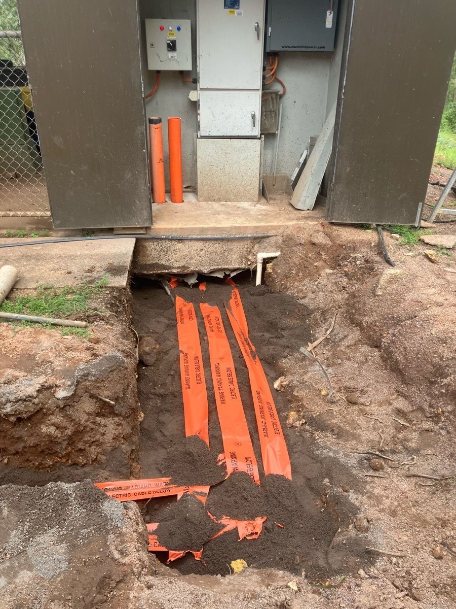 Orange utility cables in a trench leading to a wall-mounted electrical box.