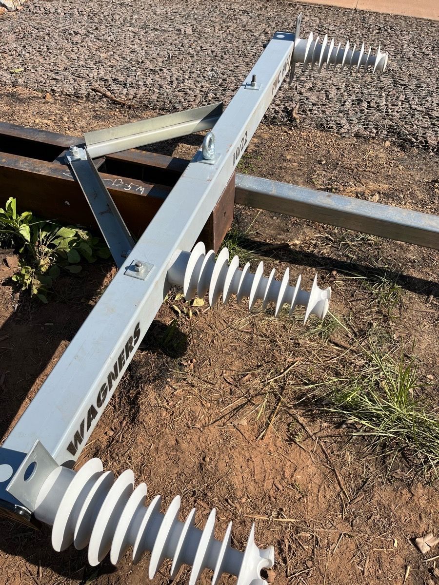 Metal farm implement with white disc blades on a dirt field, viewed from above