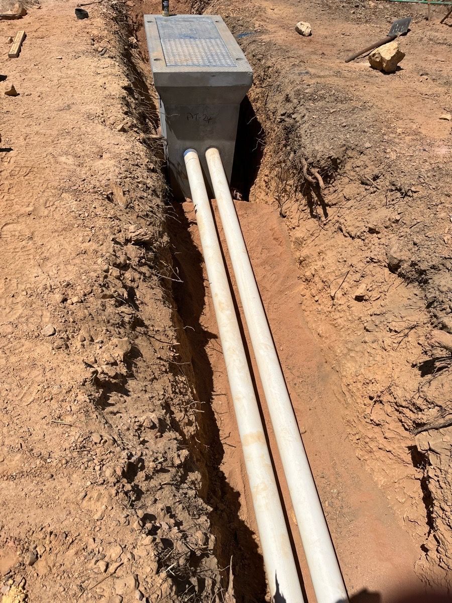 Open trench with white utility conduits leading into a gray electrical box.