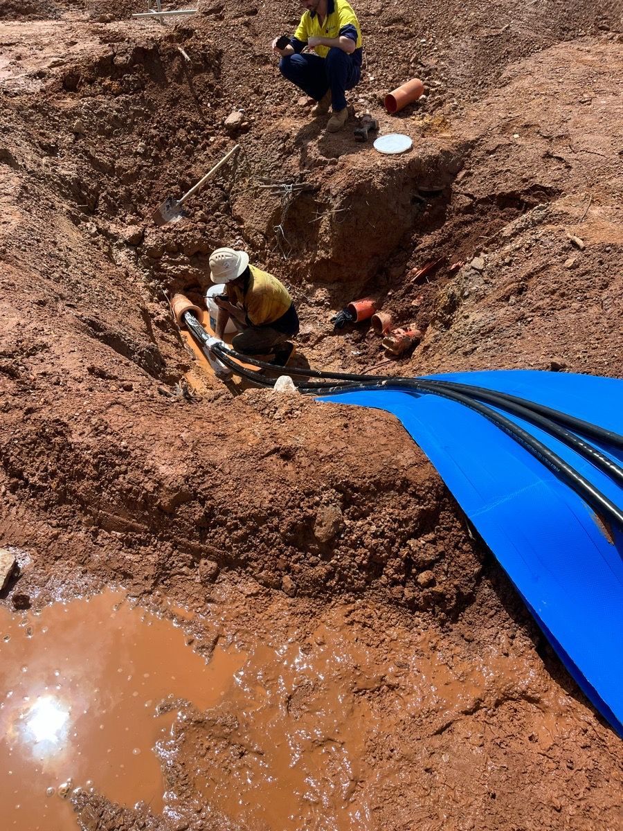 Workers in hard hats installing a large blue pipe in a muddy trench