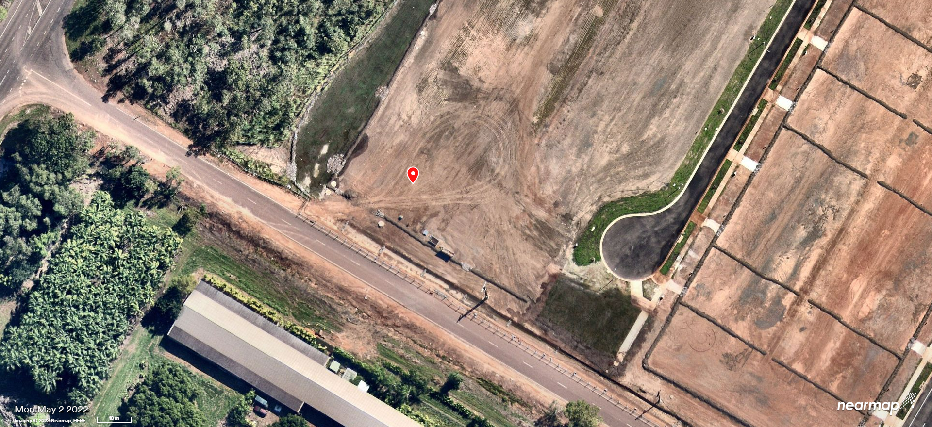 Aerial view of a rural roadside with fields, a narrow waterway, and a few buildings.