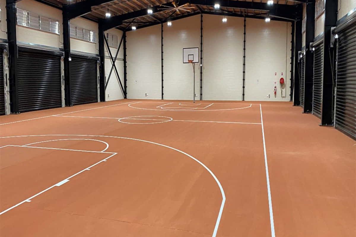 Empty indoor basketball court with orange floor, white lines, and a hoop at the far end