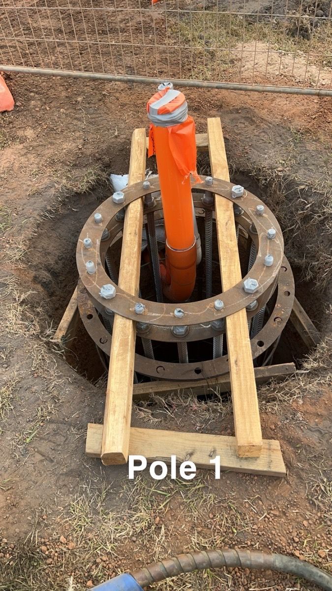 Orange utility pole secured in a dirt hole with wooden braces and a metal support ring