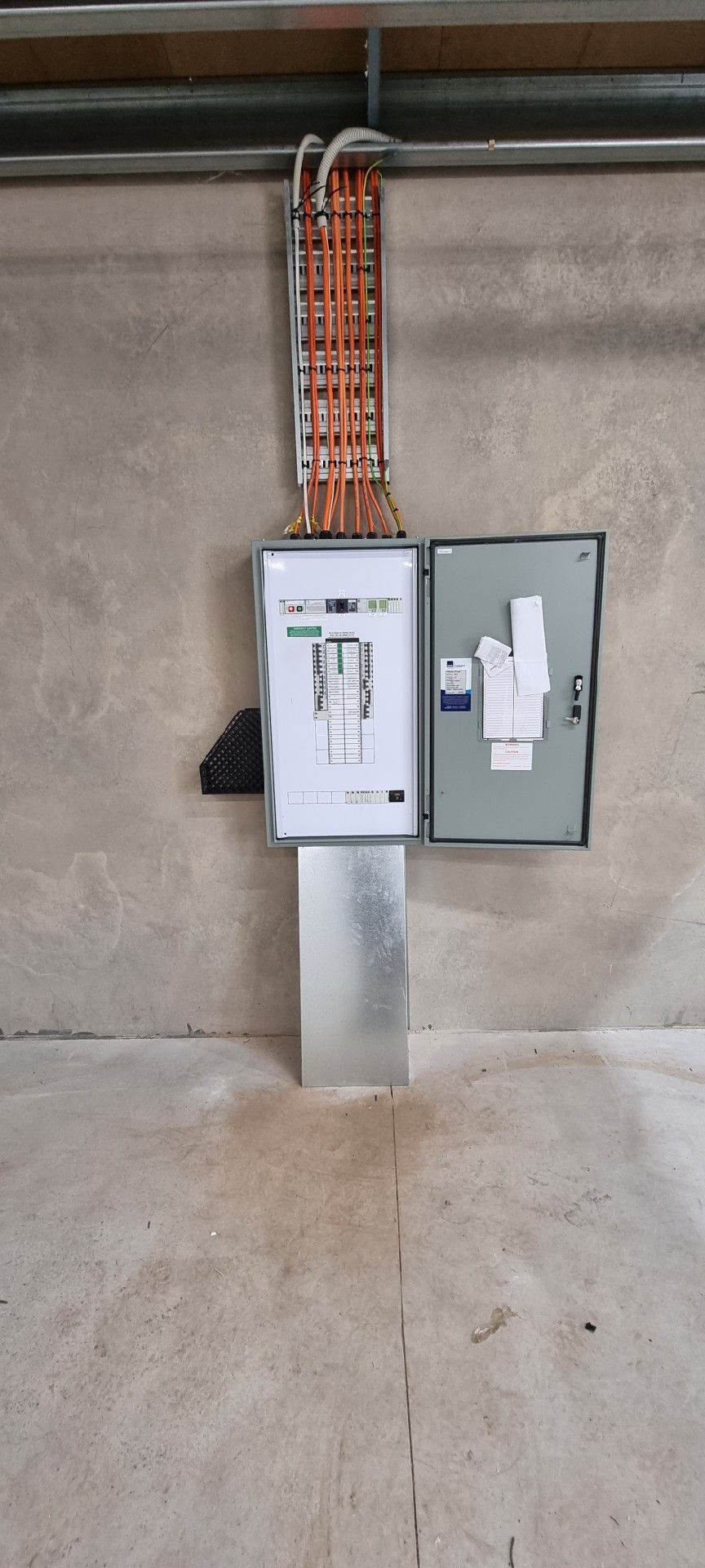Electrical panels mounted on a concrete wall with orange conduit and wiring above