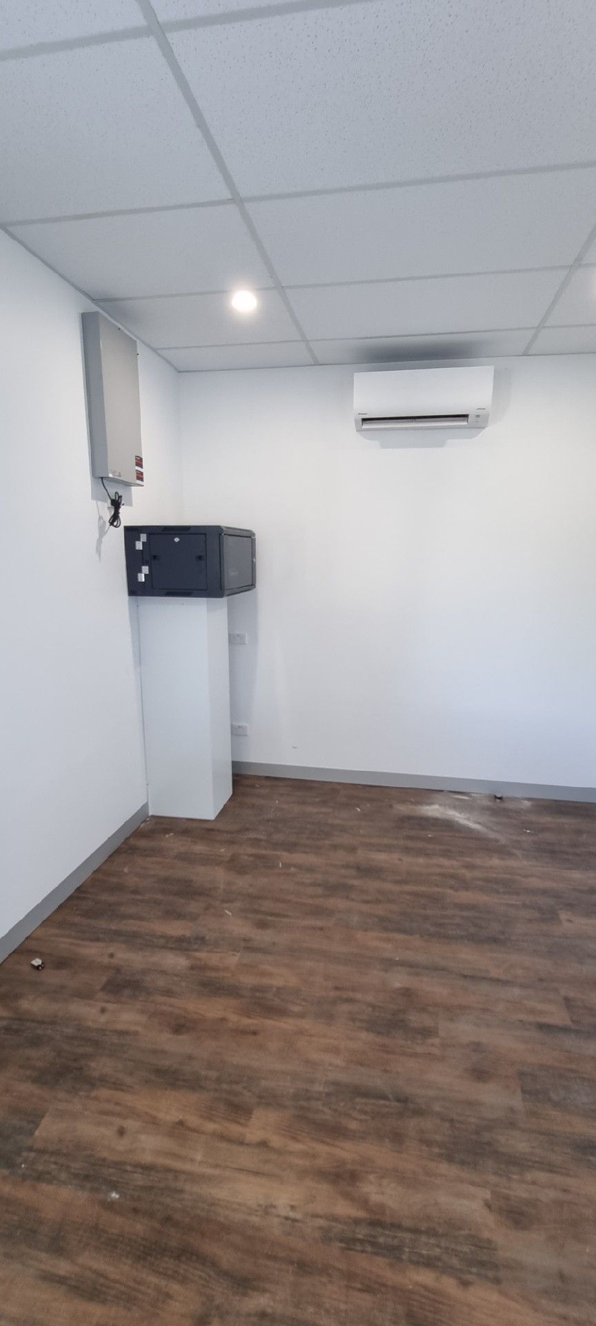 Empty white room with wood floor, ceiling lights, a wall-mounted AC, and a small cabinet in the corner
