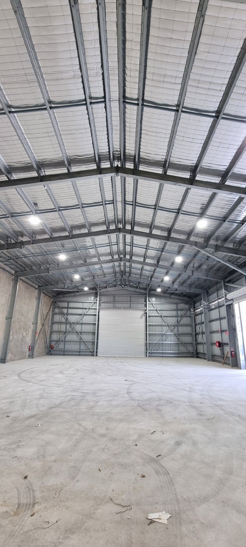 Empty warehouse interior with metal roof trusses, concrete floor, and a large closed roll-up door.