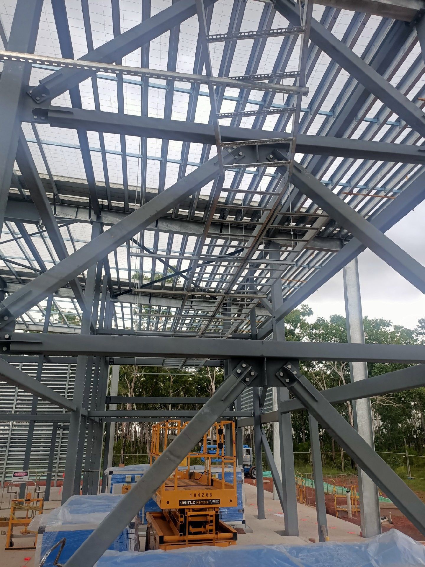 Steel building frame under construction with scaffolding, crane, and workers inside