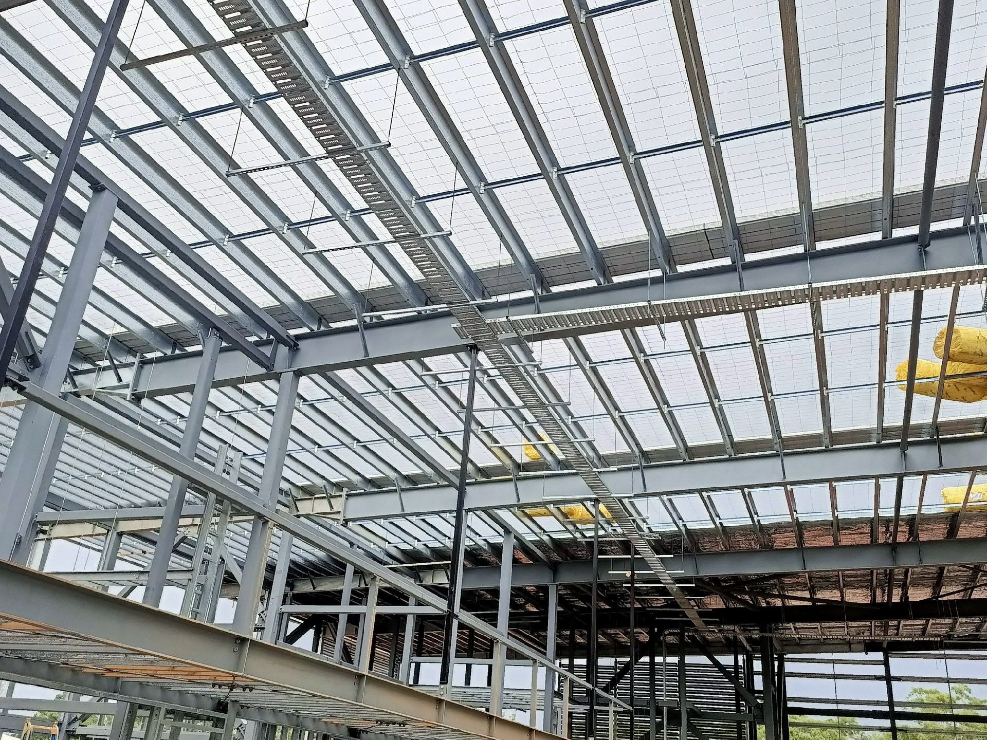 Steel-framed building under construction with glass roof panels and exposed beams