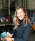 Een lachende vrouw houdt een kleurenpalet vast in een werkplaatsomgeving.