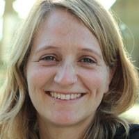 Vrouw met blond haar lacht in de buitenlucht.
