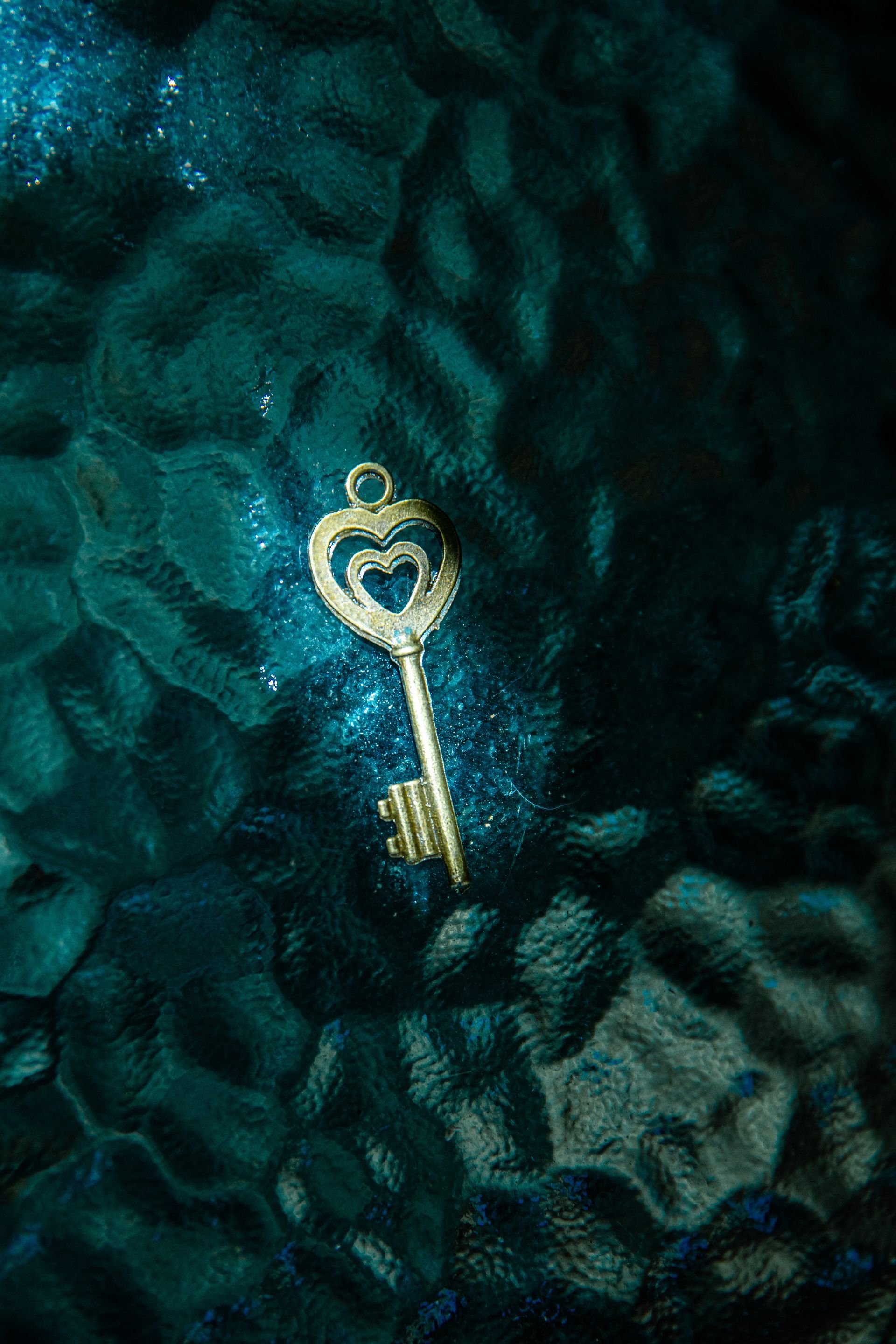 Gouden sleutel met hartvormige kop tegen een gestructureerde, donkerblauwe achtergrond met verspreide glitters.