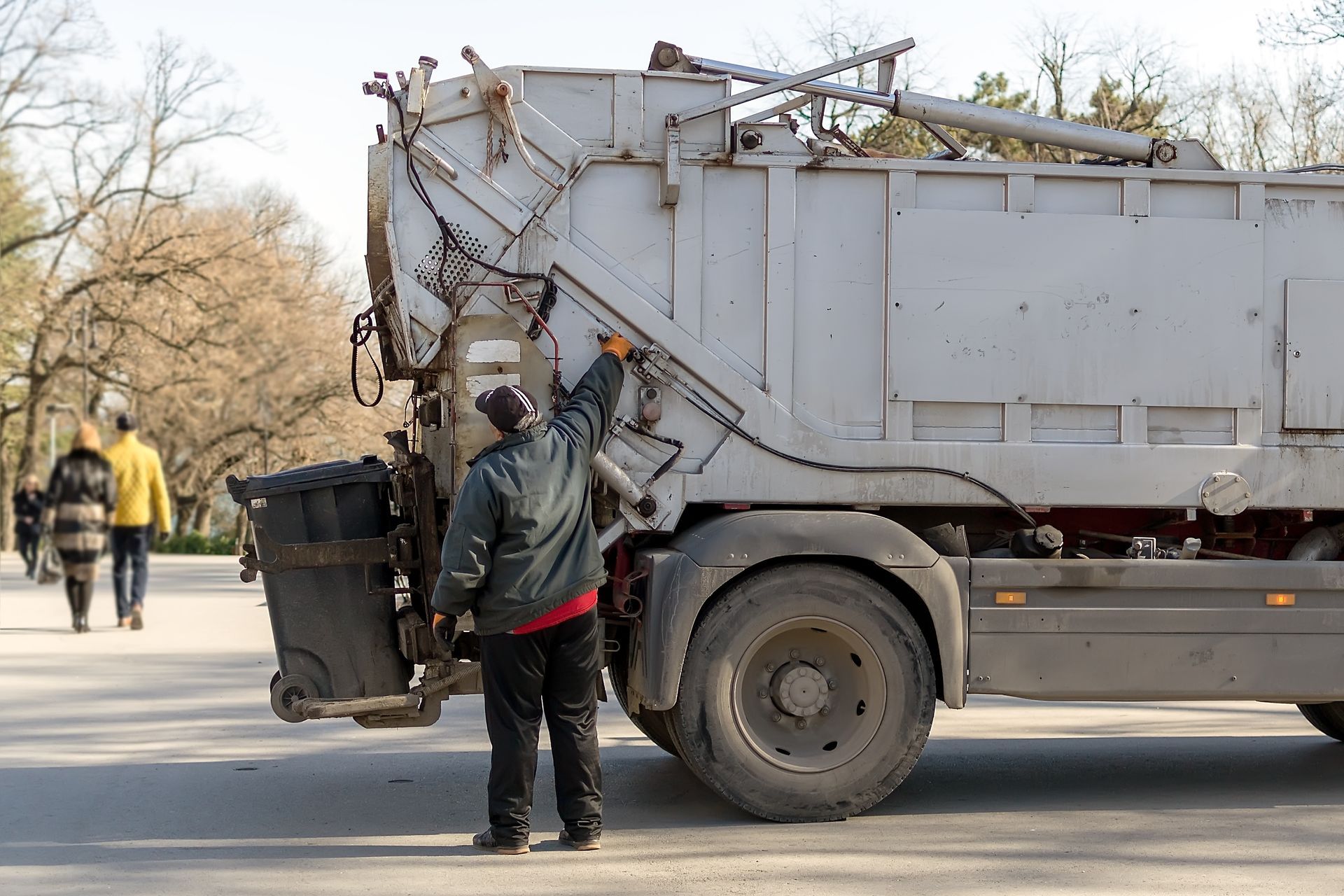 Garbage truck operator emptying a waste bin into a garbage truck during collection.