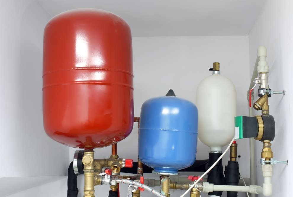 Red and blue pressure tanks with pipes and valves in a utility room