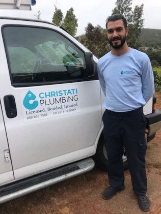 Man standing beside a white Christati Plumbing van, smiling outdoors on a dirt lot.