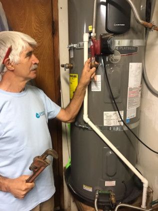 Technician inspecting a water heater with a wrench in a utility room.