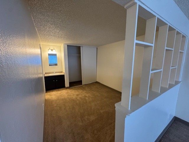 Empty carpeted room with white walls, closet, and built-in shelving beside a staircase.