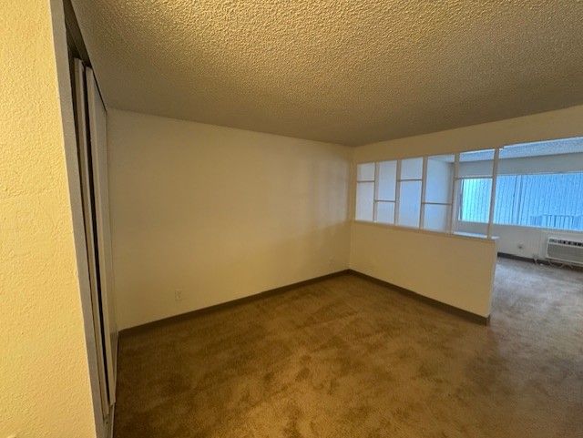Empty beige apartment room with brown carpet and a half wall overlooking a windowed living area