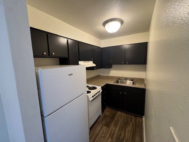Small kitchen with white appliances, dark cabinets, and wood flooring.
