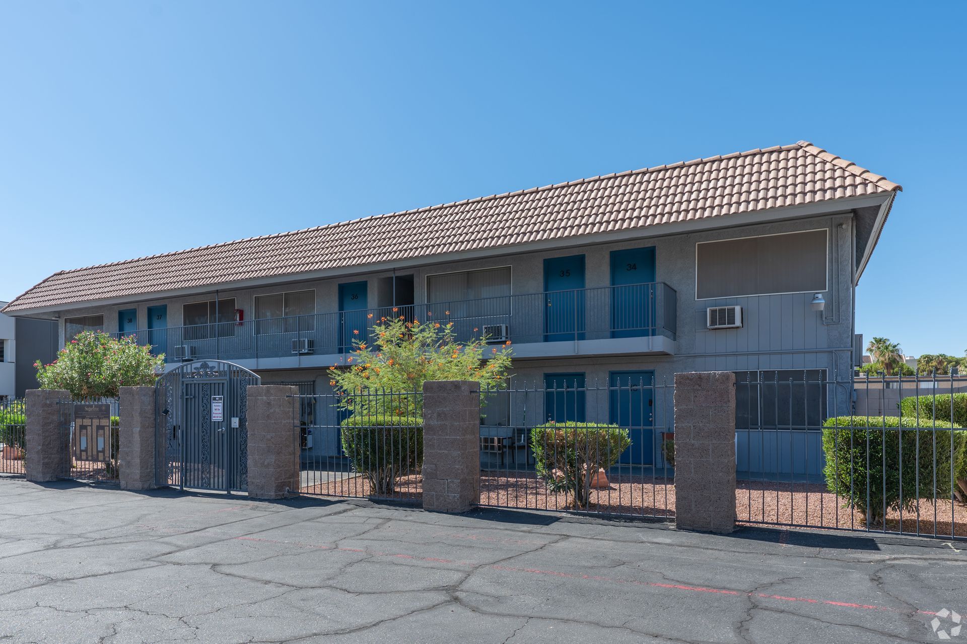 Two-story apartment building with blue shutters and a brick fence under a clear sky