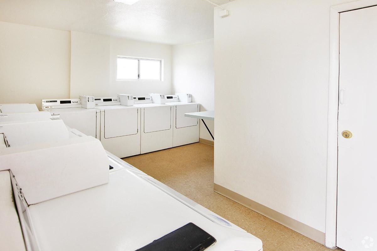 Bright laundry room with white washers and dryers along the back wall and a tan floor