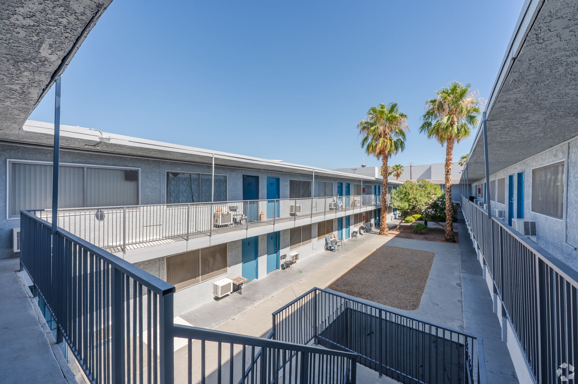 Courtyard view of a motel with blue railings, open walkways, and palm trees under a clear sky